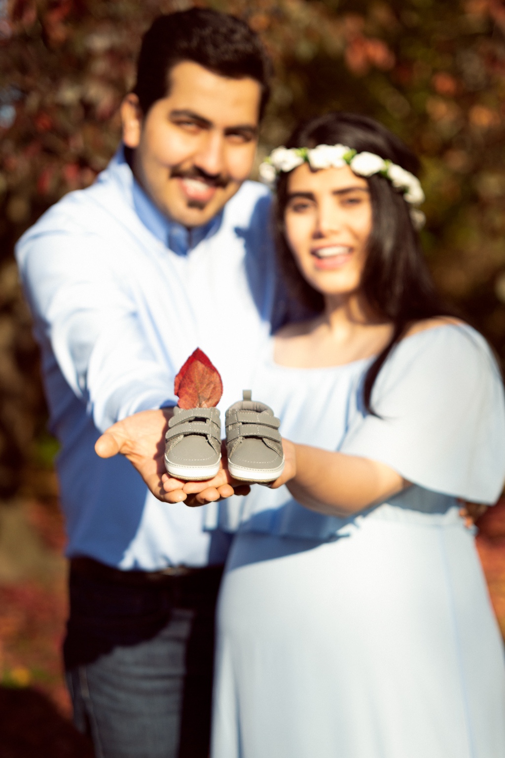Expecting couple holding a pair of baby shoes during an autumn maternity session