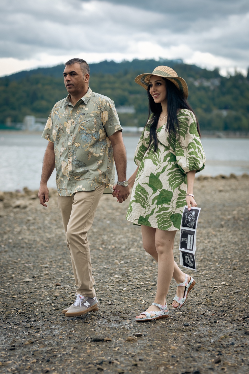 Expecting couple walking together by the lakeshore with ultrasound photographs