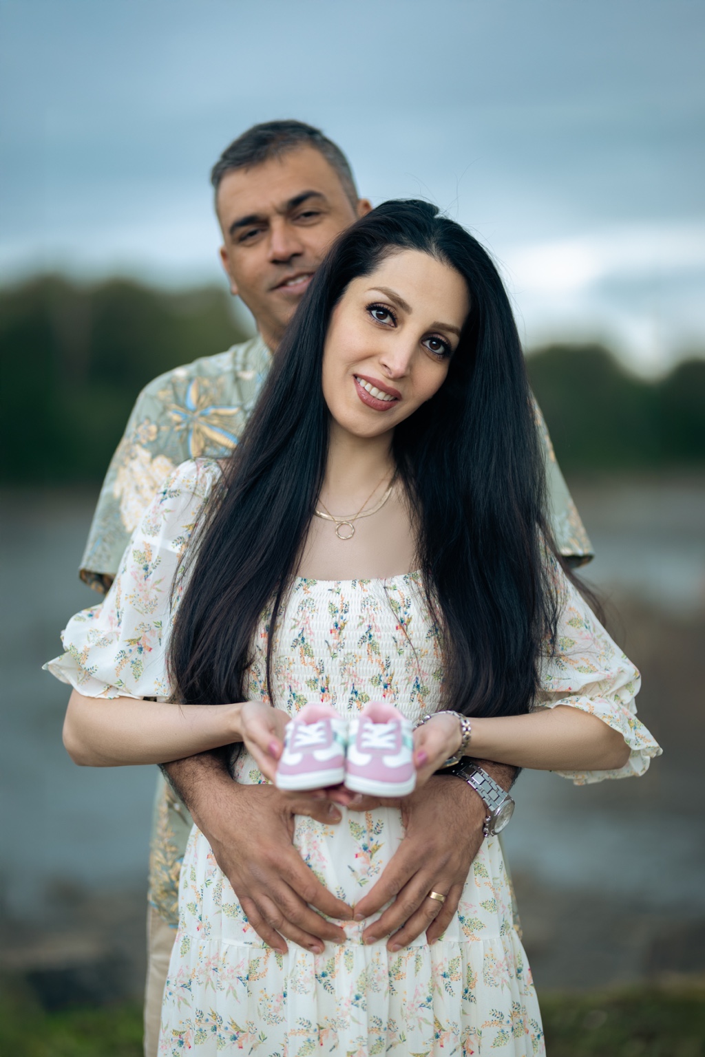 Expecting couple holding pink baby shoes over the mother’s baby bump