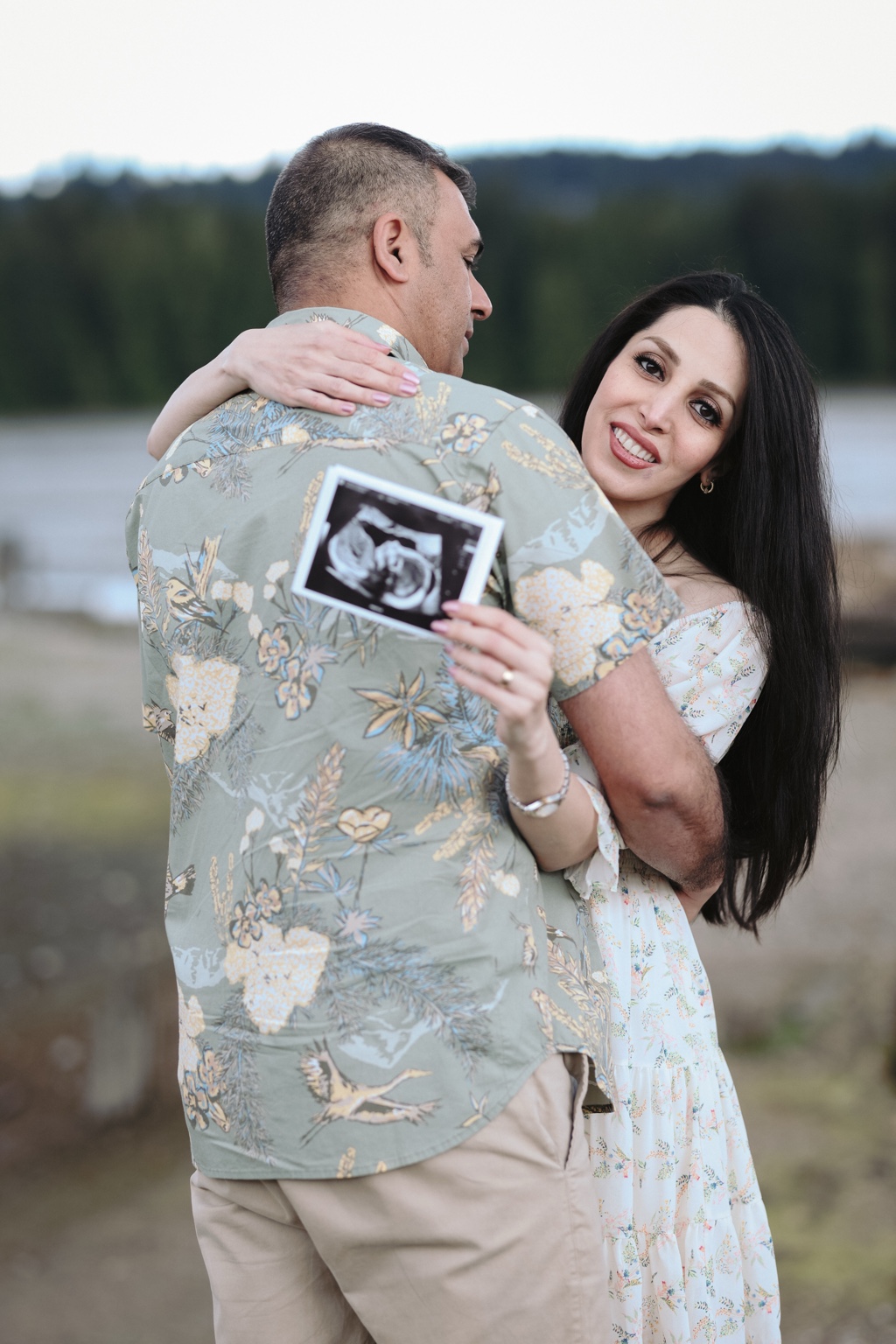 Expecting mother holding an ultrasound photograph while embracing her partner