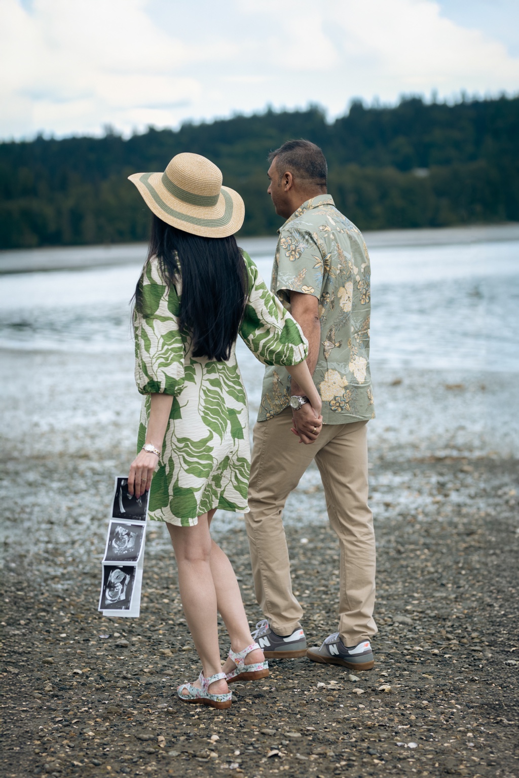 Expecting couple holding hands beside the water with their ultrasound photographs